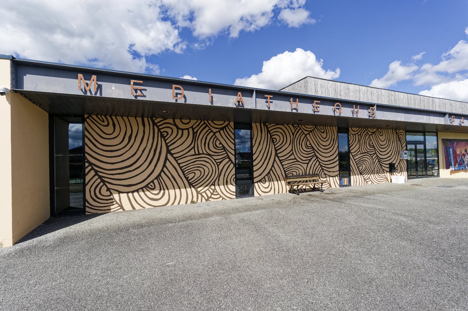 Façade de la médiathèque d'Edern habillée d'une fresque d'art pariétal : méandres et spirales inspirés des gravures du cairn de Gavrinis, peints en brun sur fond crème